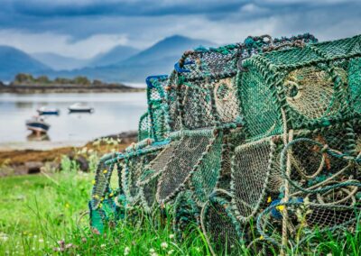 Lobster fishing pots sit by the waterside in green grass in Scotland. Used to illustrate the scottish food and drinks tours page of the turas travel website.