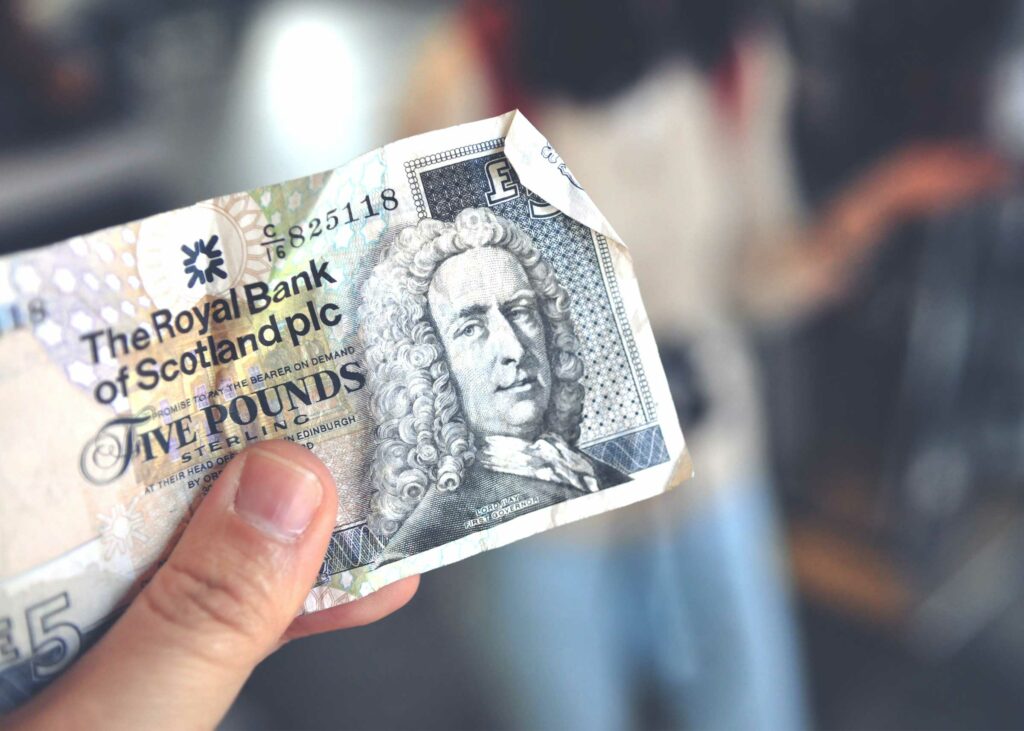 A hand holds a scottish five pound note to highlight the idea of tipping in scotland for tourists.